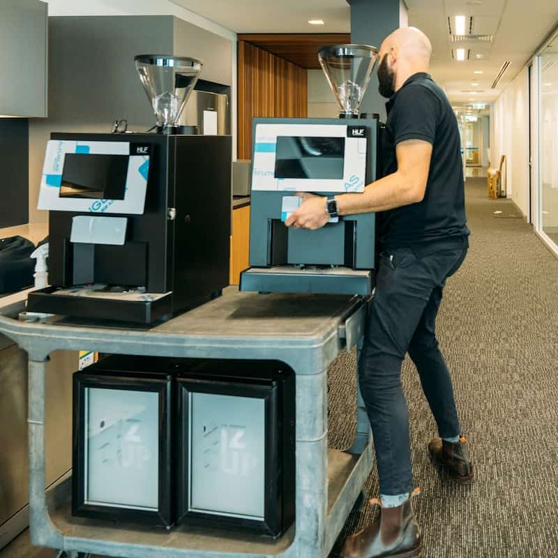 Man carrying an HLF office coffee machine in a workplace hallway